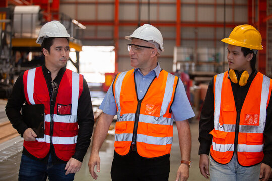 Three industrial engineers wearing safety uniform walk and discuss operations inside heavy factory, representing leadership, teamwork, and communication in high-risk industrial.