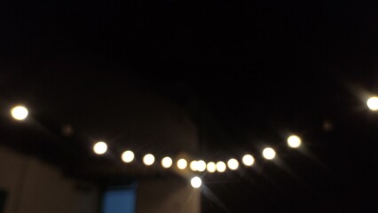 Blurry photo of glowing string lights at night, creating a soft bokeh effect and cozy atmosphere. This image is perfect for backgrounds, design projects, party themes