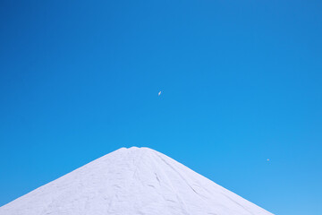 White salt mountain on clear blue sky. Salt storage and production in the Salinas de Torrevieja, Europe's largest salt producer.