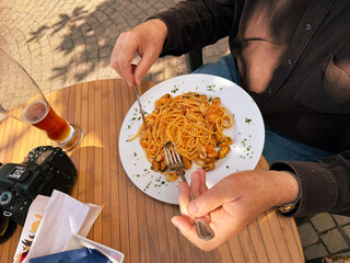 A man is sitting at a wooden table in a restaurant holding knife and fork in his hands during eating spaghetti with seafood. Healthy nutrition.