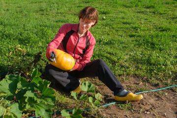 Middle-aged woman holding yellow pumpkin in her hands, looking at it and smiling. Gardening and horticulture concept