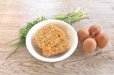 dry instant noodles on bowl with raw egg in plastic packaging and spring onion couple parsley...