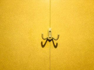 Metallic coat hook casting shadow on yellow wall