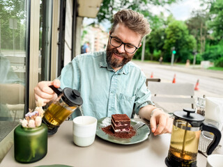 Man drinking tea with cake at outdoor cafe in urban setting. Lifestyle, leisure and social dining...