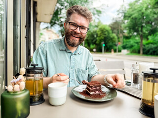 Man drinking tea with cake at outdoor cafe in urban setting. Lifestyle, leisure and social dining experience with authentic atmosphere of city cafe culture.