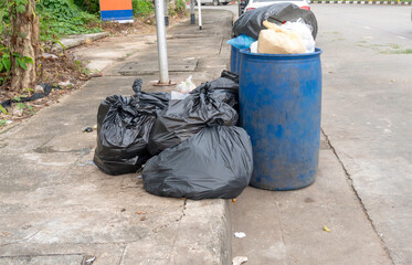 Garbage in black garbage bag and blue bins in stack at garbage dump on footpath of city street