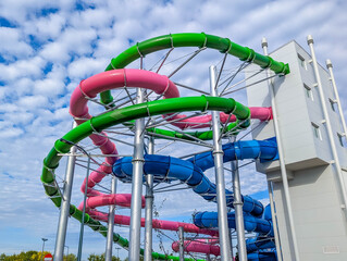 Colorful spiral water slide tower with multiple curved tubes against clear blue sky at aquatic recreation facility. High quality photograph