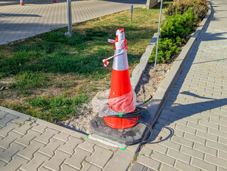 Orange traffic cone positioned on concrete pavement beside green grass area in urban public space. High quality photograph