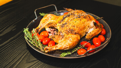 Golden brown whole roast chicken with fresh thyme and cherry tomatoes on a rustic wooden board. Top view, beautifully presented for food blogs and advertising.