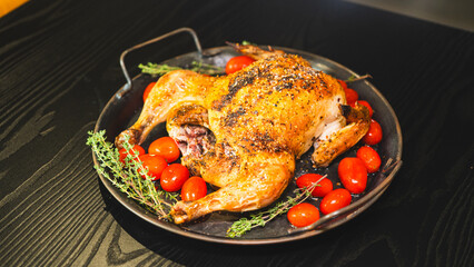 Golden brown whole roast chicken with fresh thyme and cherry tomatoes on a rustic wooden board. Top...