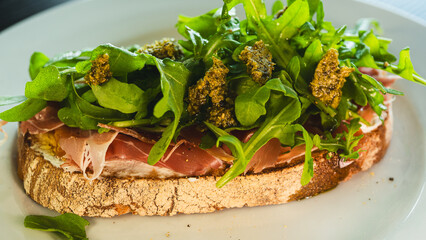 Beautifully served toast with fresh mozzarella, authentic Italian prosciutto, vibrant arugula and green pesto sauce. Perfect for food blogs and menus.