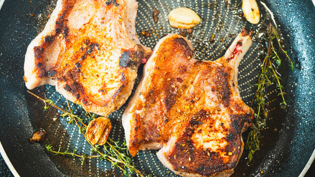 Juicy bone-in pork chops sizzling in a pan with golden fried garlic and fresh thyme sprigs. Beautifully cooked and presented for food content.