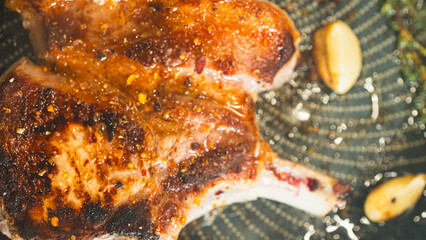 Juicy bone-in pork chops sizzling in a pan with golden fried garlic and fresh thyme sprigs....