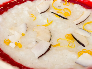 Close-up white porridge with coconut, lemon zest, and berry sauce served in a plate. Breakfast, nutrition and balanced healthy eating with hot drink.