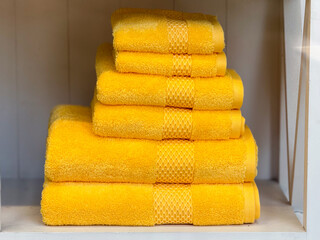 Stack of bright yellow towels in a home interior. Household textiles, cleanliness, and bathroom...