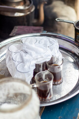 Small glasses of dark tea on a metal tray with white cloth