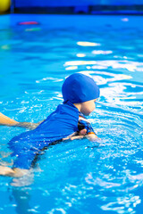 Child swimming in a pool with assistance. A young child practices swimming in a bright blue pool while being supported by an adult, enjoying the water activity.