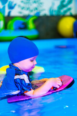 Child enjoys water play with float. A young child in a blue swim cap plays with a colorful float in a swimming pool, enjoying the water on a sunny day.