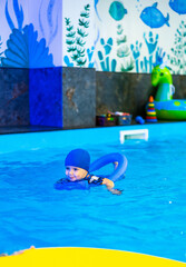 Child enjoys swimming in a colorful pool. A young child wearing a blue swim cap swims in a vibrant pool surrounded by cheerful underwater themes.