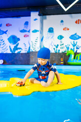 Kid with toy car in pool. A young child in a blue swimsuit enjoys playing with a toy car on a floating island in the pool.