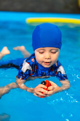 Child enjoying playtime in swimming pool. A young child in a blue swim cap and outfit floats in...