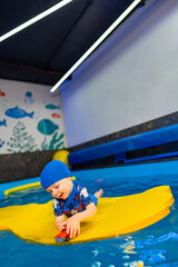 Child plays on colorful float in pool. Young child enjoys playing with a toy while floating on a vibrant yellow paddle in a swimming pool.