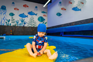 Child playing in a colorful pool area. A young child in a blue swim cap enjoys playing with toys on a bright float in a cheerful pool environment.