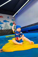 Child plays happily in water. A happy child in a blue swimming cap plays on a yellow float in a vibrant water area surrounded by aquatic decor.