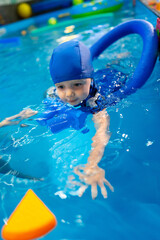 Child enjoys swimming lessons in pool. Young child participates in swimming lessons, practicing floating and swimming techniques in a bright blue pool.