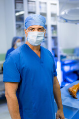 Surgeon in blue scrubs ready. A male surgeon in blue scrubs stands ready for a procedure in a...