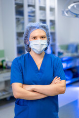 Surgeon in scrubs stands ready. A healthcare worker in blue scrubs and a mask stands with arms...