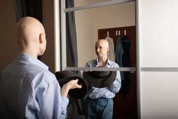 Woman standing in front of mirror holding wide-brimmed hat, concept of fashion choices,...