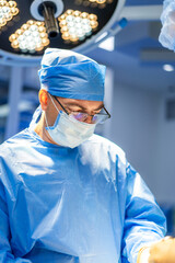Surgeon in operating room. Surgeon in scrubs, mask, and glasses concentrates on a complex operation...