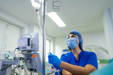 Nurse adjusting drip in hospital room. A medical professional in blue scrubs monitors an IV drip...