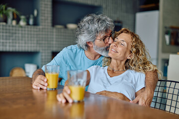 Happy retired couple enjoying a tender moment together while having orange juice at their kitchen table