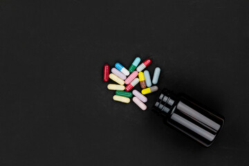Assorted colorful medicine pills and capsules spilling from a bottle on a black background. Pharmacy, healthcare, or prescription drug concept.