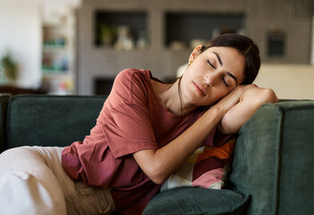 Naklejka na ściany i meble Portrait of a young woman sleeping napping on sofa and relaxing at home