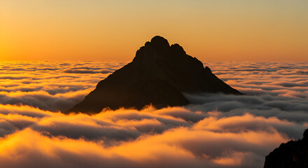 Majestic mountain peak emerges from a sea of clouds at sunset kissed by golden light and a clear