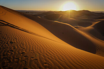 Golden hour at the Merzouga Desert showing footprints on the textured sand dunes, with the sun...