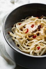 top view of creamy peanut sauce on noodles, overhead view of peanut noodles in a grey bowl
