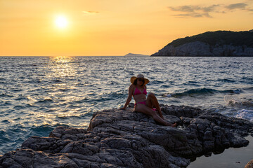 Brunette in pink bikini with straw hat at seaside during sunset in Montenegro