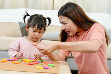Asian single mother teaching little daughter assembling colorful clay pieces into creative shapes...