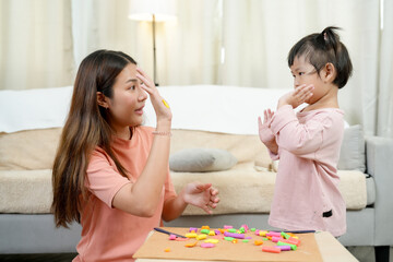 Asian single mother and little daughter learning through gesture-based play smiling during colorful...