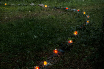 A row of glowing memorial candles placed on mossy stones in the forest, creating a peaceful path of light symbolizing remembrance and reflection.