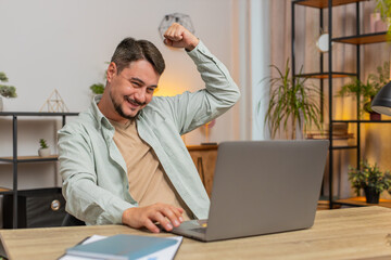 Happy young Caucasian man working on laptop netbook shocked by sudden victory, winning, goal...
