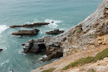 A dramatic view of jagged rock formations rising from turquoise ocean waters, with waves crashing...