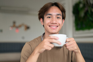 Young Thai student man holding coffee cup in cafe restaurant wearing headphones