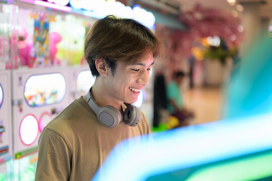 Young Thai man using vending machine in shopping mall with headphones playing games
