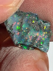 Holding up a rough chunk of opal with intense colors 