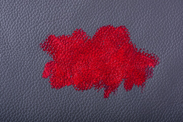 A vibrant red lipstick is being swatched on a smooth blue leather surface, highlighting the rich color and texture of both the makeup and the material beneath.